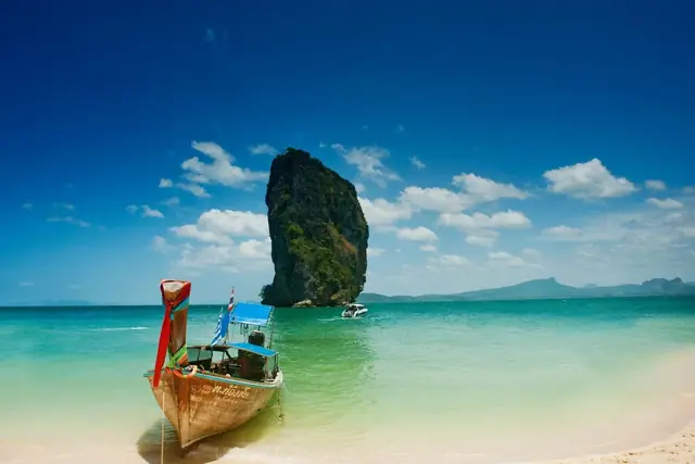 Un bateau longtail peint sur une plage de sable blanc, avec le piton calcaire de Koh Poda au large
