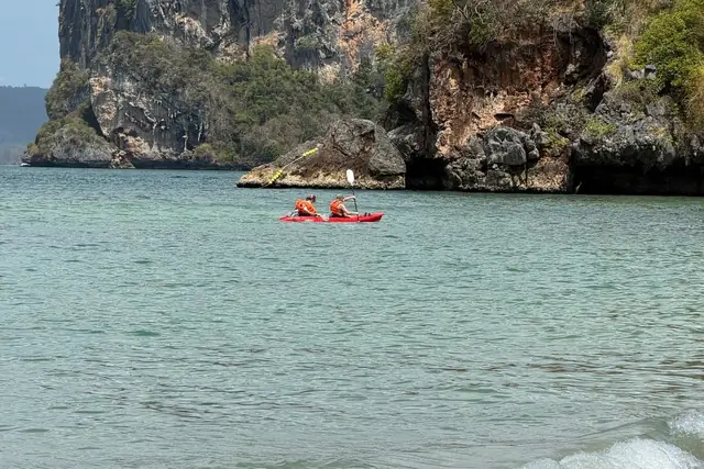 Deux personnes dans un kayak de mer rouge pagayant au pied des falaises calcaires de la côte de Krabi
