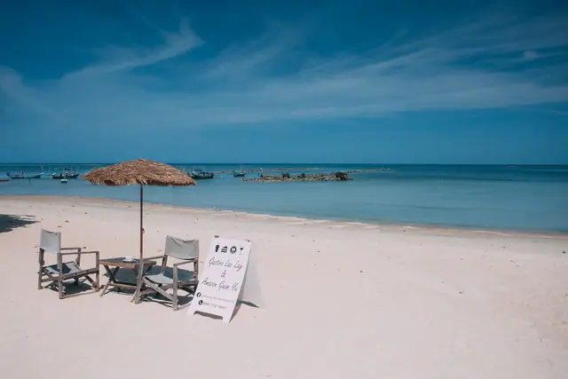 Deux transats sous un parasol de paille sur une plage de sable blanc déserte