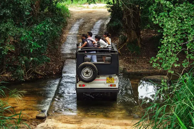 A 4x4 full of passengers crossing a stream on a jungle track