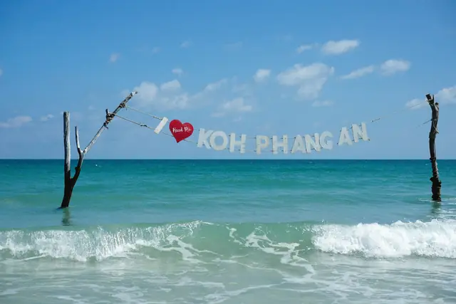 Un panneau « Koh Phangan » tendu entre deux poteaux dans les vagues
