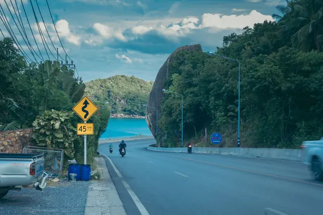 A scooter on a winding coastal road with a glimpse of the sea, Koh Samui