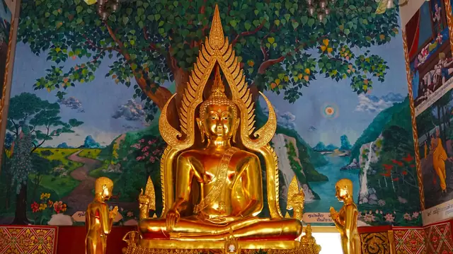 A gilded seated Buddha before a painted tree mural inside a temple hall